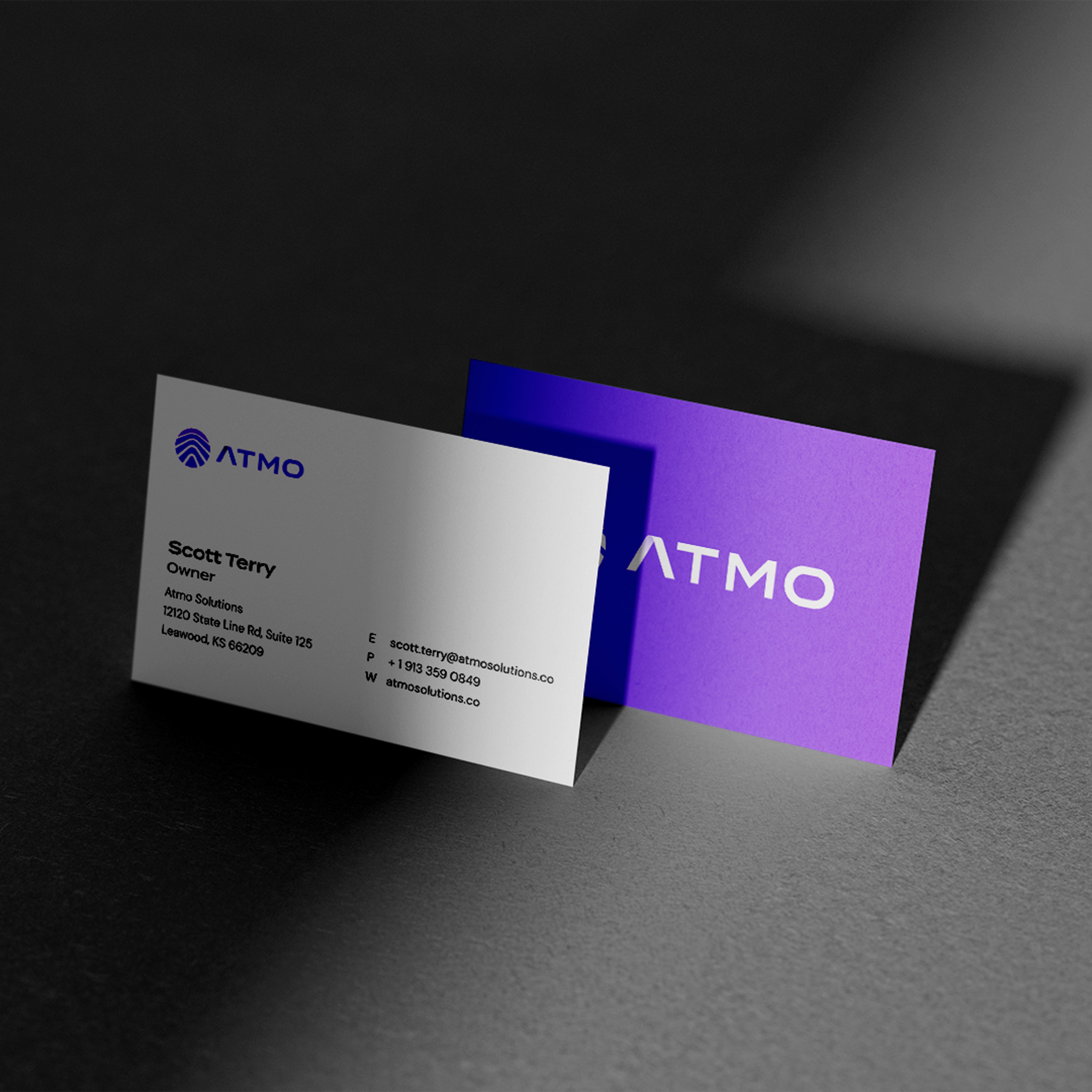 Two business cards in strong contrasting light being propped up, one showing the front design of the card and one showing the back of the card.